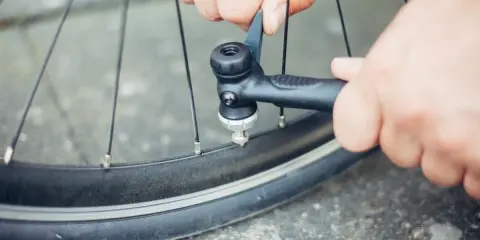 Hände pumpen mit einer Handpumpe Luft in ein Fahrradventil.