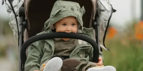 Maluch w wózku, w zielonej kurtce z misiem, gryzie pałąk. To urocze babciowe chwile.