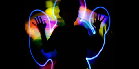 Silueta de niño jugando con light painting, creando auras de colores vibrantes a su alrededor.