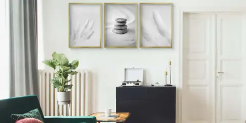 Trzy minimalistyczne plakaty w złotych ramach nad ciemną komodą. Dowiedz się, jak powiesić plakat bez niszczenia ścian.