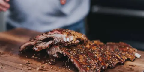 Saftige, gewürzte 321 Ribs liegen auf einem Holzbrett. Hände im Hintergrund bereiten sie für den Genuss vor.