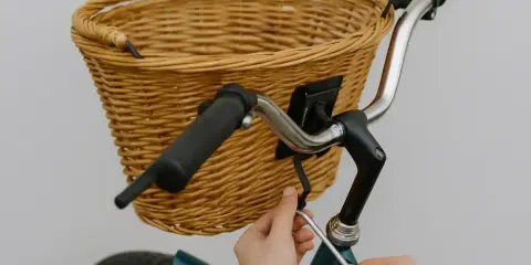 Instrukcja: jak zamontować koszyk do roweru click. Ręce dokręcają śrubę mocującą wiklinowy koszyk do kierownicy.