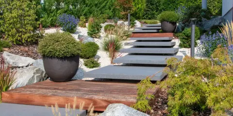 Escalier moderne en pierre et bois menant à un jardin paysager sans entretien, avec des graminées ornementales et des arbustes.