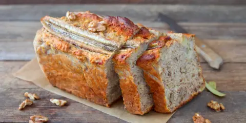 Pyszny chlebek bananowy z bakaliami, pokrojony w kromki, z widocznymi orzechami i bananem na wierzchu.