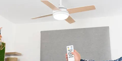 Mano con mando a distancia operando un ventilador de techo escayola con luz integrada.