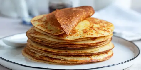 Una pila di dorate crepes senza glutine, una piegata in cima, su un piatto bianco.