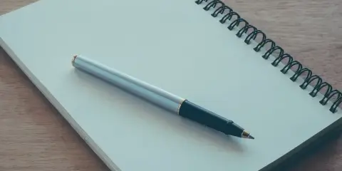 Notes for a podanie o pracę leżą na drewnianym blacie. Długopis czeka na rozpoczęcie pisania.