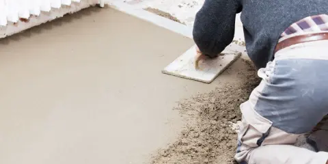 Operaio stende il massetto con una spatola, mostrando la differenza tra massetto e calcestruzzo grezzo.