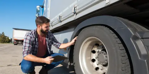 Hombre revisa neumático de camión con portapapeles. Se pregunta cuanto se tarda en sacar el carnet de camión.