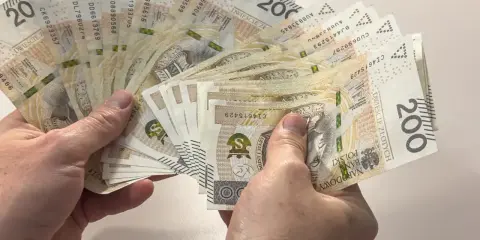 Dłonie trzymają wachlarz banknotów 200 zł. Zastanawiasz się, ile to brutto, jeśli 4200 netto to Twoja pensja?