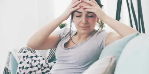 Kobieta z rękami na skroniach, wyrażająca ból głowy, być może objaw psychosomatyki.