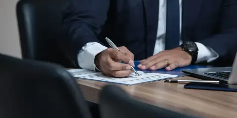 Adwokat w garniturze pisze długopisem na dokumencie przy biurku.