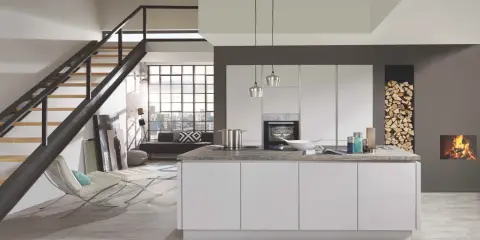 Cuisine moderne avec îlot central blanc. Le mur gris foncé contraste avec les meubles blancs et le bois de chauffage.