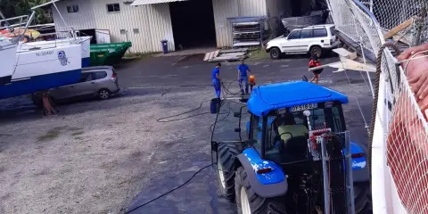 Tracteur bleu près d'un bateau, peut-être pour le prix d'entretien d'un bateau de 7m. Des ouvriers travaillent.