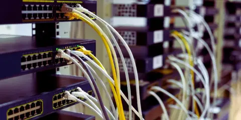 Faisceau de câblage RJ45 b, avec des câbles blancs, jaunes et gris connectés à des commutateurs réseau empilés.