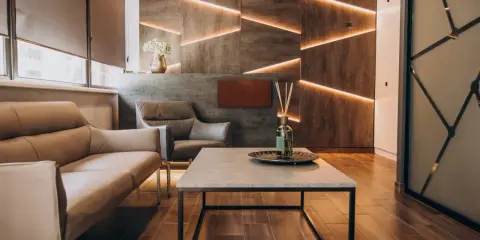 Nowoczesne wnętrza z betonową ścianą i geometrycznym podświetleniem. Skórzane sofy i stolik kawowy tworzą przytulną przestrzeń.