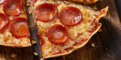 Pyszna pizza na tortilli z pepperoni, roztopionym serem i chrupiącym spodem, podana na drewnianej desce.