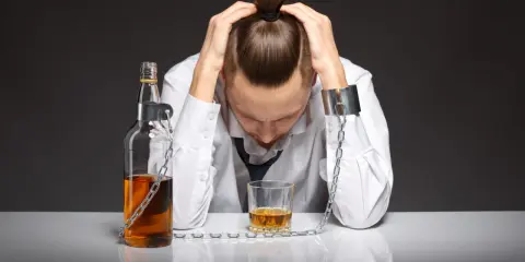 Zrozumienie, że podsumowanie terapii alkoholowej to klucz do wolności. Mężczyzna w kajdanach, przykuty do butelki i kieliszka.