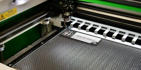 Macchina per taglio laser in azione, che realizza un cartello "Ascenseur" con simboli per bagni. Perfetta per progetti di taglio laser personalizzati.