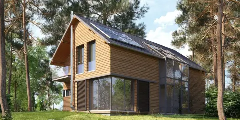 Maison en bois moderne avec panneaux solaires, conçue par un constructeur maison écologique. Entourée de pins, elle s'intègre parfaitement à la nature.