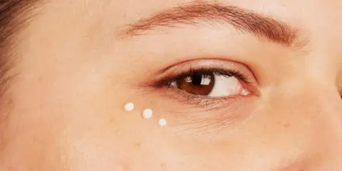 Trois petites perles de crème sont appliquées sous l'œil, montrant comment appliquer contour des yeux pour une peau hydratée.