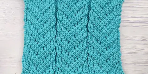 Muestra de tejido azul turquesa con patrón de espiga en dos agujas. Las hebras forman un diseño entrelazado que recuerda a espigas de trigo.