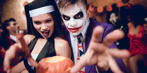 Un couple en costumes effrayants, une nonne et le Joker, profite d'une **soirée costumée** d'Halloween, tenant une citrouille sculptée.
