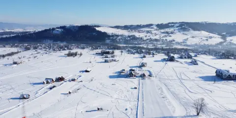 Zimowy krajobraz z wyciągiem narciarskim Horników Wierch u Goryla. Śnieg pokrywa pola i dachy domów, tworząc malowniczy widok.