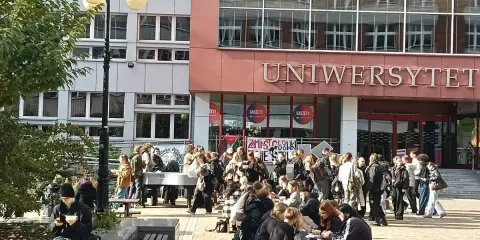 Grupa studentów przed budynkiem z napisem "UNIWERSYTET". Zastanawiasz się, czym się różni akademia od uniwersytetu?