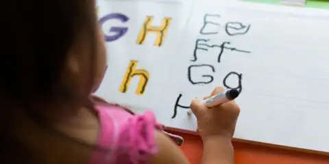 Dziecko uczy się, jak się pisze h, ćwicząc litery na tablicy.