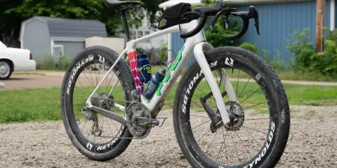 Biały rower gravelowy z szerokimi oponami i sakiewką na kierownicy, gotowy na przygodę. Czy to gravel czy szosa, zależy od terenu!