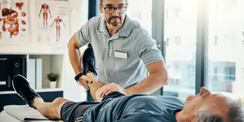 Fizjoterapeuta ćwiczy nogę starszego pacjenta. Rehabilitacja jest kluczowa, by dowiedzieć się, komu przysługuje szpital uzdrowiskowy.