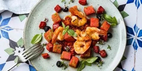 Saftige argentinische Rotgarnelen mit Wassermelonenwürfeln, Tomaten und Basilikum auf einem Teller.