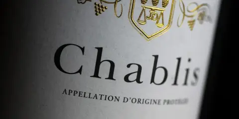 Nahaufnahme eines Etiketts mit der Aufschrift "Chablis". Ein goldenes Wappen mit Trauben und Waage ziert das Etikett dieses Chablis Weins.