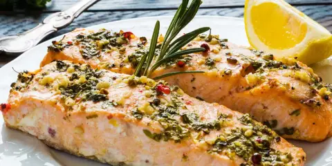 Två saftiga laxfiléer med en härlig pesto-topping, garnerade med rosmarin och en citronklyfta.