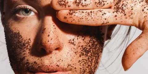 Visage couvert de grains d'un exfoliant chimique naturel, une main cache un œil.