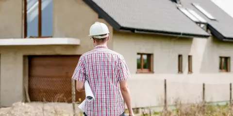 Inżynier w kasku z planami w ręku analizuje kosztorys inwestorski budowy domu.
