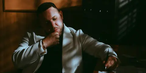 Louis Villain, wiek nieznany, w białej marynarce, zamyślony, siedzi przy biurku.