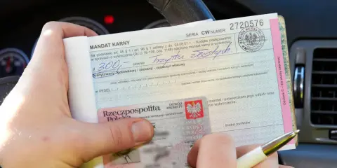 Ręka trzyma mandat karny na kwotę 300 zł. Obok dowód osobisty. Jak uniknąć mandatu? Uważaj na drodze!