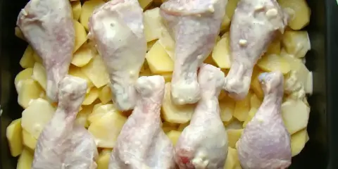 Osiem pałek kurczaka w sosie, ułożonych na plastrach ziemniaków w brytfannie. Idealne do pieczenia, by uzyskać chrupiące pałki z kurczaka w piekarniku.