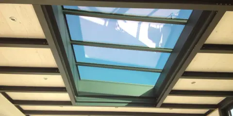 Veranda avec un grand puit de lumière vitré, illuminant un plafond en bois et poutres métalliques.