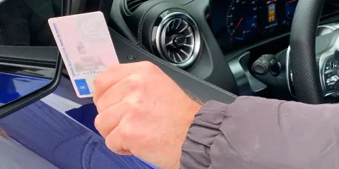 Mano sujetando permiso de conducir español dentro de un coche moderno, anticipando la conducción autónoma en España.
