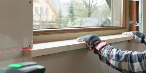 Montaż nowego parapetu wewnętrznego w bloku. Czerwona linia lasera pomaga w precyzyjnym ułożeniu drewnianego elementu.