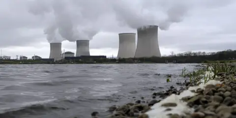Kühltürme eines Atomkraftwerks mit Dampfschwaden über einem Flussufer.