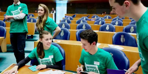 Jongeren in groene shirts met 'Nationaal Jeugdparlement' opdruk, discussiëren in de Tweede Kamer. Ze pleiten voor stemrecht naar 16 jaar.
