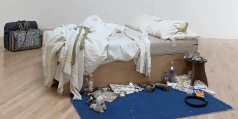 La cama deshecha de Tracey Emin, rodeada de objetos personales, botellas y maletas, evoca una historia de vida.