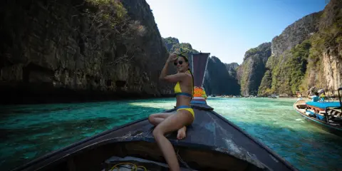 Kobieta w bikini na łodzi, podróżująca po turkusowej wodzie między klifami. Idealne miejsce na wakacje na własną rękę.
