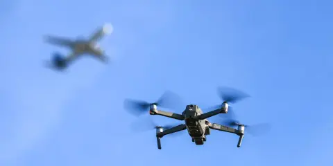 Drohne im Flug, während ein Flugzeug im Hintergrund verschwimmt. Informiere dich über Länder, in welchen Ländern Drohnen verboten sind, bevor du abhebst.
