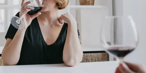 Kobieta z krótkimi blond włosami pije czerwone wino. Czy zastanawiasz się, jak hashimoto a alkohol wpływają na zdrowie?