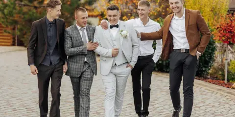 Pięciu mężczyzn w eleganckich strojach, idealnych na wesele. Podpowiedź, jak ubrać się na wesele jako gość mężczyzna.